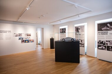 Exhibition in a bright room with display panels and a model car on a pedestal. | © Nikolaus Faistauer Photography