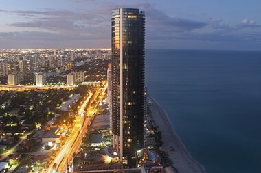 Skyscraper by the coast at sunset, illuminated streets and ocean in the background. | © Studio F. A. Porsche
