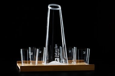 Elegant clear glass carafe with matching glasses on a wooden tray against a dark background. | © Zell am See-Kaprun Tourismus
