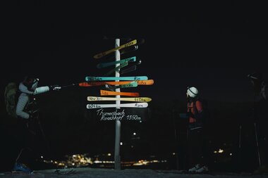 Night scene of ski tourers at Ronachkopf evening tour, preparing their skis on a signpost. | © Zell am See-Kaprun Tourismus