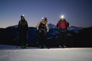 Three people ski touring at dusk with mountain landscape in the background | © Zell am See-Kaprun Tourismus