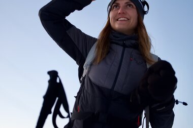 Person on an evening ski tour in the mountains, wearing a headlamp, looking upward, equipped with skiing gear. | © Zell am See-Kaprun Tourismus