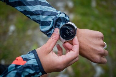 Person checking a digital sports watch during a trail run in nature. | © Suunto Philipp Reiter