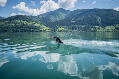 Person swimming in a lake with mountains in the background on a sunny day. | © Suunto Philipp Reiter