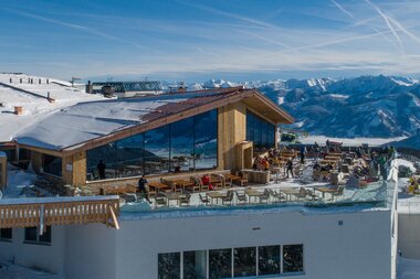 A modern restaurant with wood and glass design on a snow-covered mountain terrace overlooking the mountains. | © Schmittenhöhebahn AG