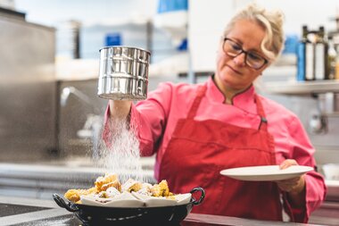 Person sprinkling powdered sugar on Kaiserschmarrn in a kitchen. | © Zell am See-Kaprun Tourismus