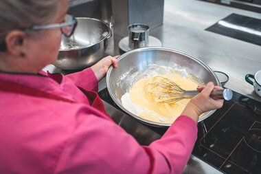 Person preparing Kaiserschmarrn, stirring the batter in a bowl in a modern kitchen. | © Zell am See-Kaprun Tourismus