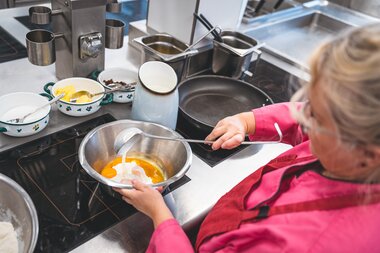 Person preparing Kaiserschmarrn in a kitchen setting with eggs, flour, and cooking utensils. | © Zell am See-Kaprun Tourismus