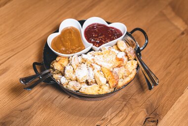 Kaiserschmarrn served on a plate with powdered sugar, accompanied by two heart-shaped bowls of sauce, one with jam and the other with a curry sauce. | © Zell am See-Kaprun Tourismus