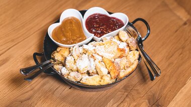 Kaiserschmarrn served on a plate with powdered sugar, accompanied by two heart-shaped bowls of sauce, one with jam and the other with a curry sauce. | © Zell am See-Kaprun Tourismus