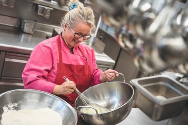 Person preparing Kaiserschmarrn in a professional kitchen, using cooking utensils and large bowls. | © Zell am See-Kaprun Tourismus