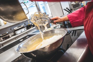 Person stirring a Kaiserschmarrn in a pan while cooking in a kitchen. | © Zell am See-Kaprun Tourismus