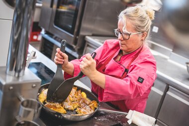 Person cooking Kaiserschmarrn in a kitchen, using a spatula, wearing a pink chef jacket. | © Zell am See-Kaprun Tourismus