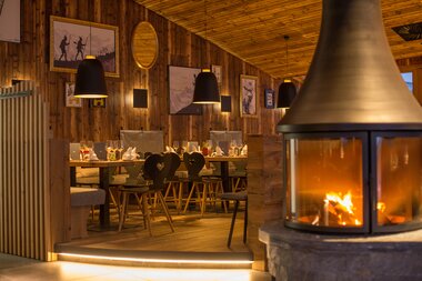 Cozy restaurant with wood decor, a warming fireplace, and a set table inside. | © Schmittenhöhe