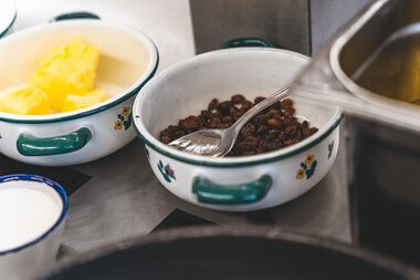 Ingredients for Kaiserschmarrn, including raisins and melted butter, in bowls on a kitchen counter. | © Zell am See-Kaprun Tourismus