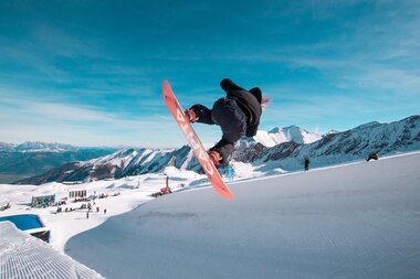 Skateboard rider performing a jump on snow at Kitzsteinhorn with mountains in the background. | © Kitzsteinhorn