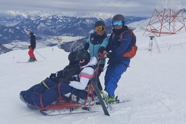 People engaging in adaptive skiing on snowy mountain terrain, with rescue personnel assisting during winter sports. | © Up adaptive sports 