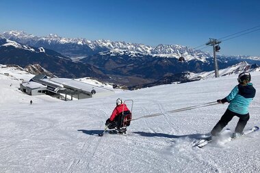 Skier on a snowy slope with mountains and ski lifts in the background on a sunny day. | © Up adaptive sports 
