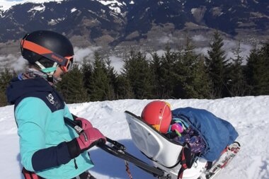People skiing adaptively on a snowy slope with mountains in the background. | © Up adaptive sports 