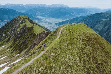 Hiking trail on green mountains with a view of the Alps and a hiker walking along the path. | © Kitzsteinhorn