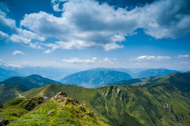 Mountain landscape with green hills and a cloudy sky, view over peaks and valleys in the distance. | © Zell am See-Kaprun Tourismus