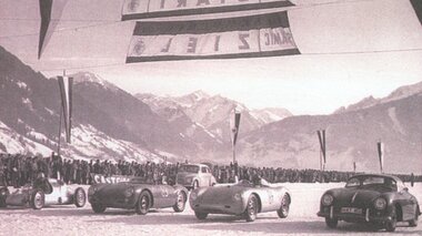Historical photo of an ice race with several cars, start and finish banners, and mountain scenery in the background. | © Zell am See-Kaprun