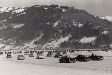 Historical image of an ice race on a frozen surface with multiple cars in motion, in front of a mountain landscape. | © ÖAMTC