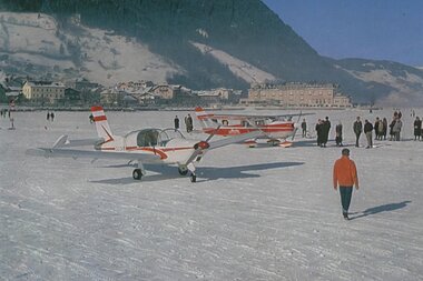 Iceplanes or passenger aircraft on a snowfield with people in the background, mountains, and a town in the background. | © Zell am See-Kaprun