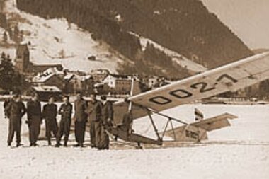 Historical photo of gliders near an aircraft on a lake, with mountains in the background. | © Zell am See-Kaprun