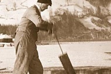 Person cutting ice at a frozen lake, with snowy mountains in the background. | © Zell am See-Kaprun