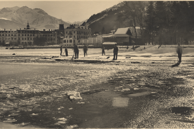 Old sepia photo of a winter scene on a frozen lake with people, mountains, and buildings in the background. | © Zell am See-Kaprun