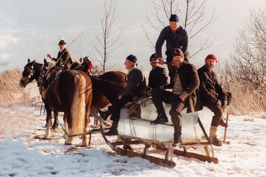 Group of people on a sled in a snowy winter landscape, some wearing traditional clothing. | © Zell am See-Kaprun