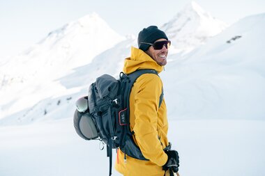 Hiker in snowy mountain landscape wearing a yellow jacket, black hat, and backpack. | © ABS Sports + Protection GmbH & Co. KG