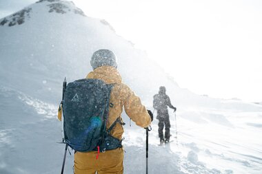 Two skiers on a snowy mountain trail in winter, with a mountain summit in the background. Snowy weather, snowshoeing.
