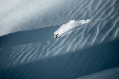 Skier descending a snow-covered slope, demonstrating speed and action on a steep trail.