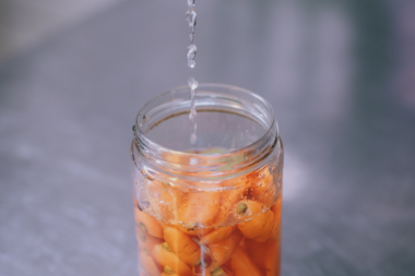 A jar with pickled peaches being filled with water.