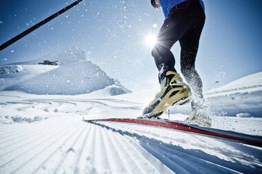 Cross-country skier on a glacier in bright sunlight, gliding through snow. Focus on the skis and energetic movement. | © ideenwerk werbeagentur gmbh