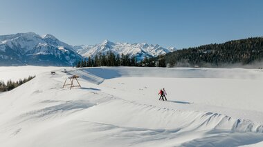 Winter scene on the Schmittenhöhe with snowshoe hikers against mountains and clear sky | © Zell am See-Kaprun Tourismus