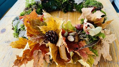 Autumn wreath made of dried leaves, twigs, moss, and small pinecones on a wooden table. | © Zell am See-Kaprun Tourismus
