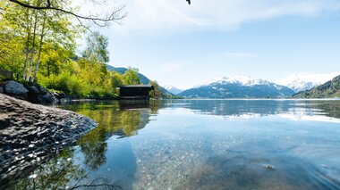 Peaceful lakeside camping site with mountain views, water, trees, sky, and a bird flying above, set in natural surroundings. | © Zell am See-Kaprun Tourismus