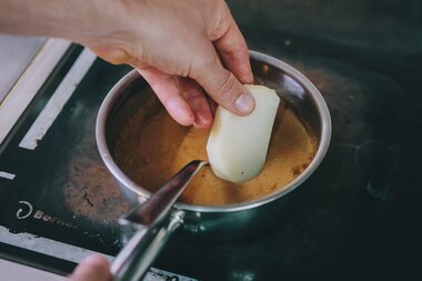 Hand holding a spoon and adding a slice of cheese into a pan with hot liquid on a stove. | © Zell am See-Kaprun Tourismus