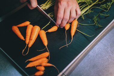 Someone cuts fresh carrots on a black table, likely during a culinary event in Zell am See-Kaprun. | © Zell am See-Kaprun Tourismus