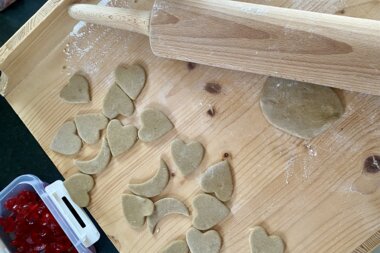 Making heart-shaped gingerbread dough on a wooden table with a rolling pin and a container of cherries. | © Zell am See-Kaprun Tourismus