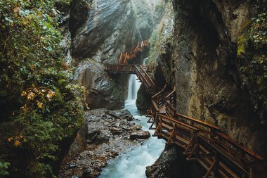 Trail along a waterfall in a narrow canyon with rocks and green trees. | © manueldietrichphotography
