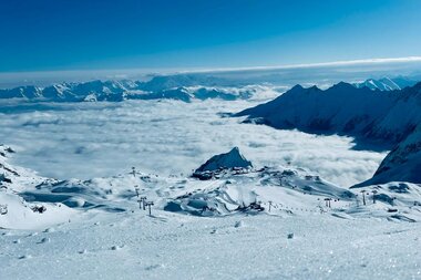 Snow-covered mountains and ski area at Kitzsteinhorn during sunrise, with a view over clouds and clear sky. | © Zell am See-Kaprun Tourismus
