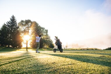 Golf players on the green at sunset, surrounded by trees, with golf equipment. | © Zell am See-Kaprun Tourismus_JOE