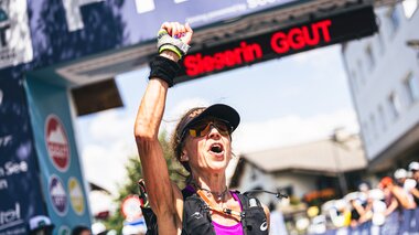 Winner of an ultra-marathon celebrating at the finish line, with banners and spectators in the background. | © Zell am See-Kaprun Tourismus
