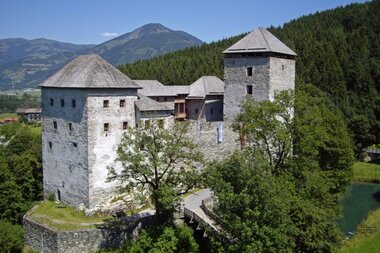 Exterior view of a medieval castle in Kaprun, surrounded by green trees and mountains. | © Burg Kaprun 