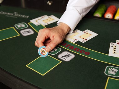 Close-up of a casino blackjack table with a hand placing a betting chip. | © Casinos Austria