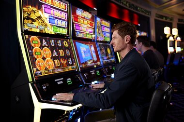 A person playing a slot machine in a casino with bright screens and gambling symbols. | © Casinos Austria